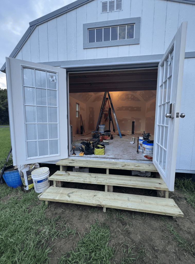 Doors open to give a view of the inside of a shed that's being plastered and painted